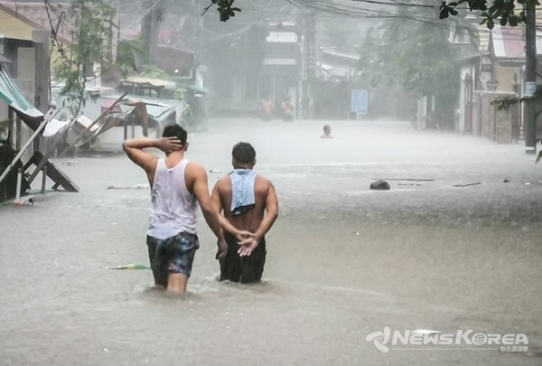 현지시간 수요일(2024년 7월 24일) 퀘손 시티 노발리체스의 팔메라 홈에서 허벅지 높이의 홍수를 헤치며 걷는 두 주민. @뉴스코리아 이창호 특파원