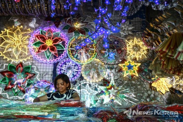 마닐라의 다피탄 아케이드에서 불이 켜진 크리스마스 랜턴이 뒤에 걸려 있는 동안 상인이 장식품을 정리하고 있다. @Joan Bondoc